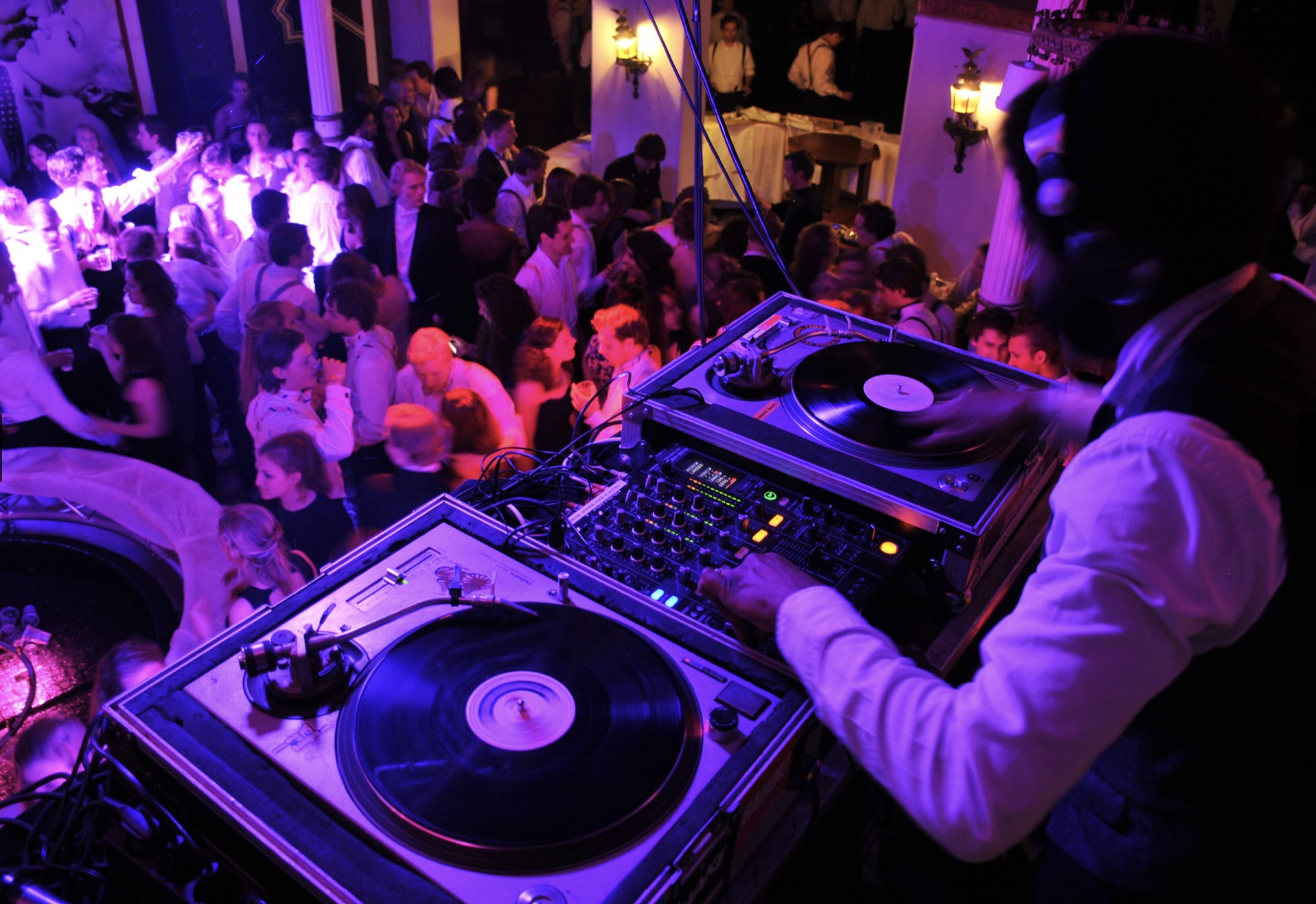 DJ mixing live on turntables above a packed party dance floor